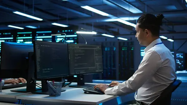 Egy adatrögzítő férfi dolgozik számítógépe előtt, háttérben szerverekkel.