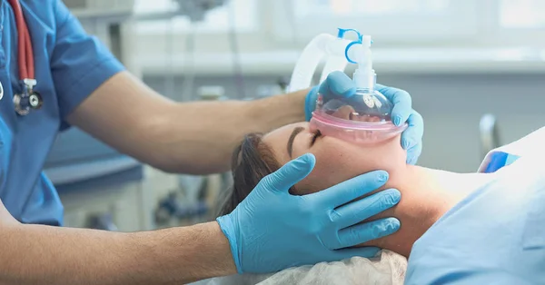 Egy aneszteziológus oxigénmaszkot helyez egy páciensre műtét közben.