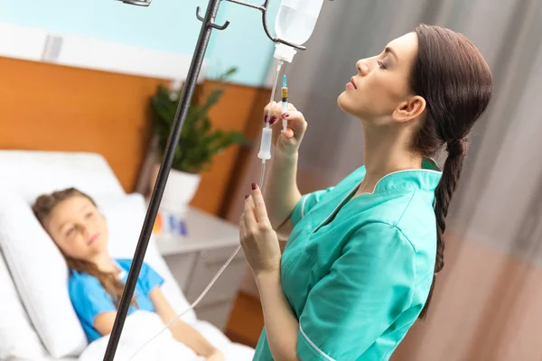Egy ápoló infúziós kezelést végez egy gyermekbetege mellett.