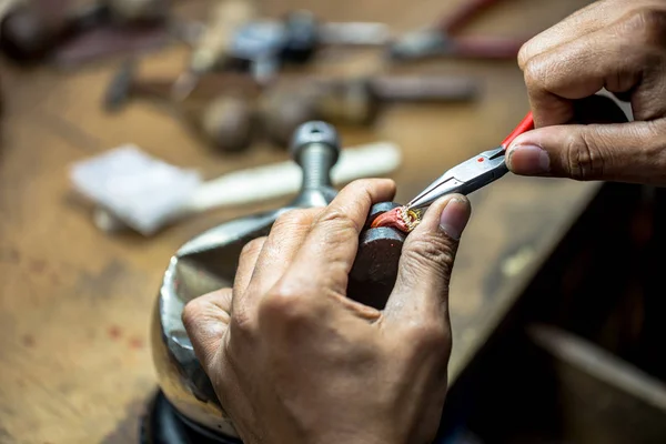Egy aranyműves precíziós munkát végez, ékszerekhez használva szerszámokat.