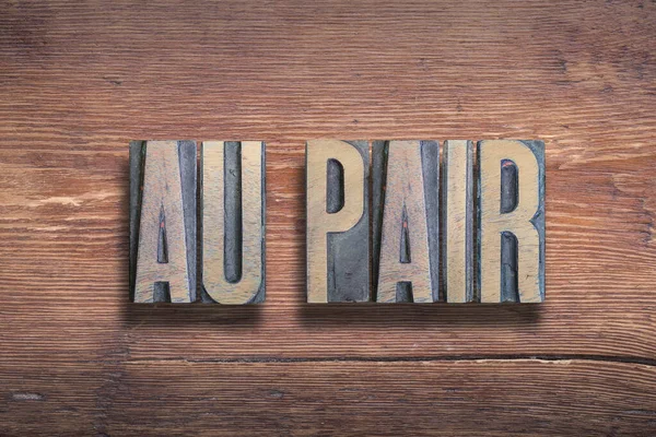 Fából készült betűk, amelyek az 'au pair' szót formálják, egy rusztikus felületen.