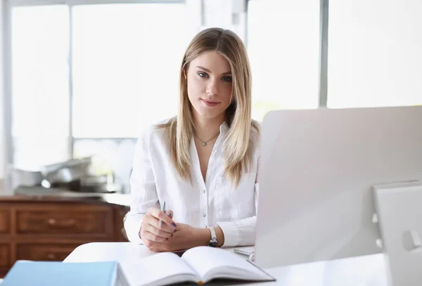 Egy fiatal nő ül az íróasztalánál, figyelmesen dolgozik a számítógépén.