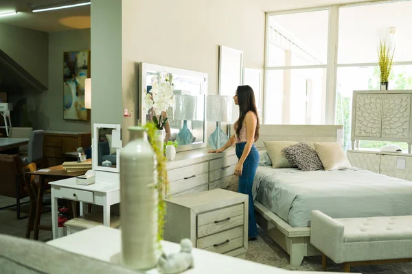 Egy nő bútorboltban nézelődik, modern bútorok között, lakástextilek mellett.