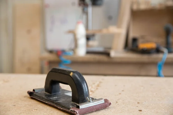 Egy bútorjavító szerszáma, csiszoló a munkapadon, háttérben műhely.