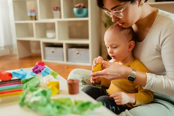 Csecsemő- és kisgyermeknevelő játszik egy kisgyerekkel, színes gyurmával.