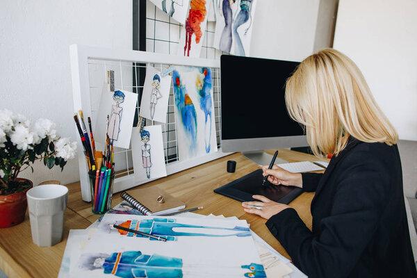 Egy divattervező grafikus táblán dolgozik, körülötte tervezési vázlatok és színes ceruzák.