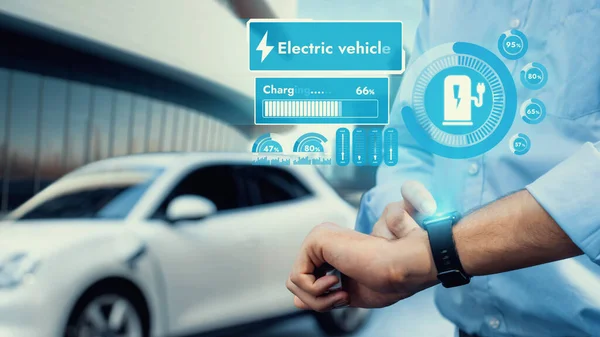 Egy férfi okosóráján ellenőrzi az elektromos jármű töltöttségi szintjét.
