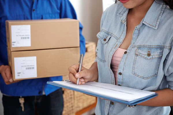 Egy fiatal nő aláír egy dokumentumot, miközben csomagokat kap.