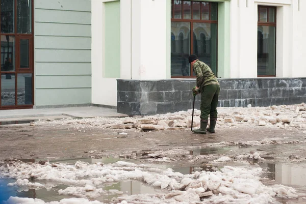 Egy gondnok a járdát takarítja, jéggel borított területen dolgozik.