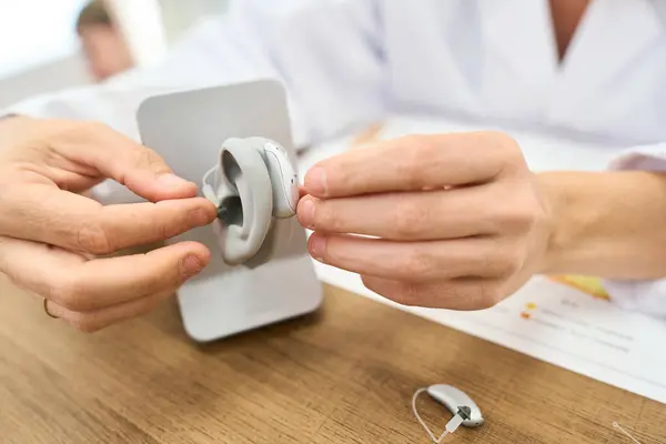Audiológiai asszisztens hallókészülék beállítását mutatja egy fülmodell segítségével.