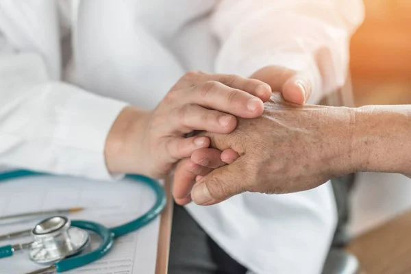 Háziorvosi asszisztens segít egy idős betegnek, kezüket fogják.