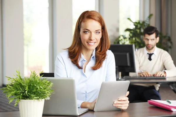 Egy HR-asszisztens mosolyogva dolgozik laptopján egy irodában.