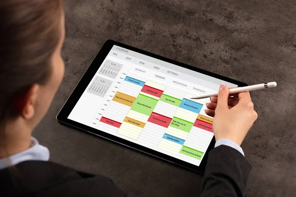 Egy nő egy táblagépen programot tervez, színes naptárbejegyzésekkel.