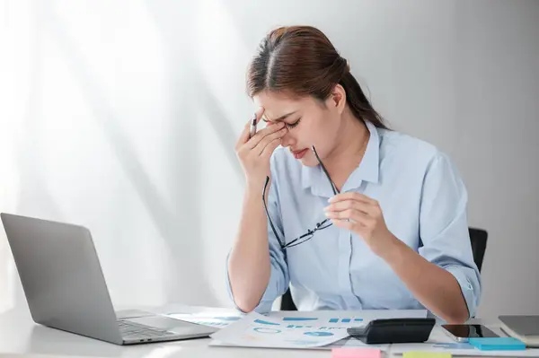 Egy banki könyvelő stresszesen számol a számítógép előtt, papírok között.