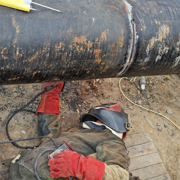 Egy csővezeték-szerelő dolgozik egy nagy cső javításán, védőfelszerelésben.