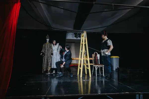 Díszletezők és színészek egy színházi előadás próbáján, jelmezekkel és kellékekkel.