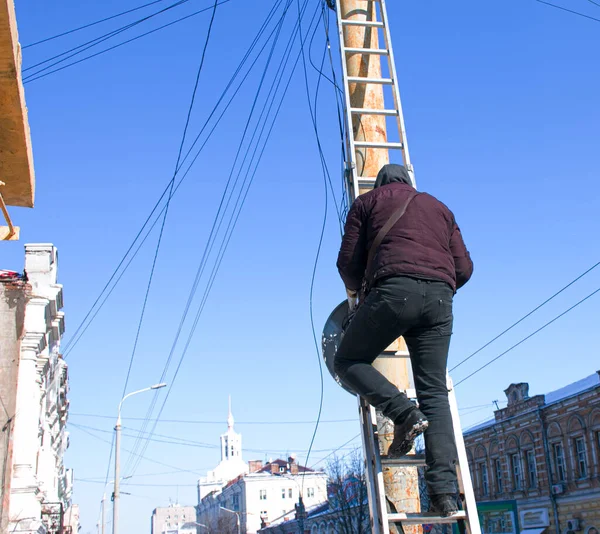 Egy elektromoshálózat-szerelő létrán állva javítja az elektromos vezetékeket.