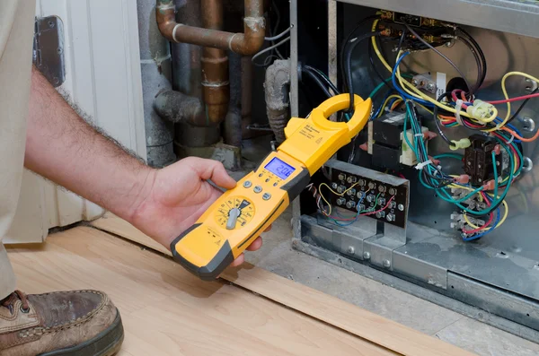 Egy épületgépész műszerrel ellenőrzi a kompresszor áramfelvételét.