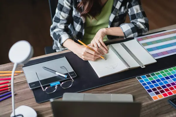 Egy grafikus nő ceruzával rajzol egy vázlatot a jegyzetfüzetében.